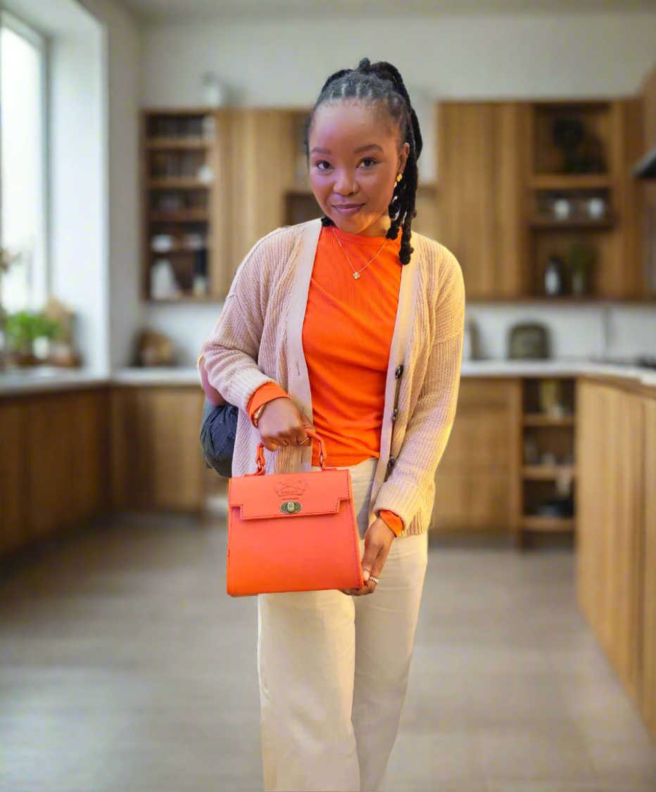A woman holding Lawrene designer bag in orange colour in a store setting with shelves and products in the background.