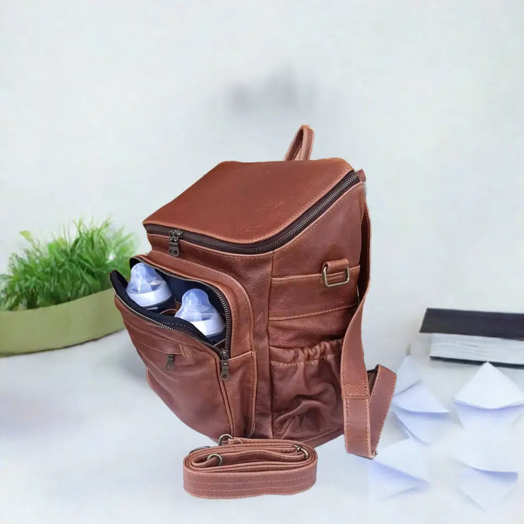 A beautiful baby backpack in Pecan tan colour made by Cape Masai Leather with 2 baby bottles in the front pocket