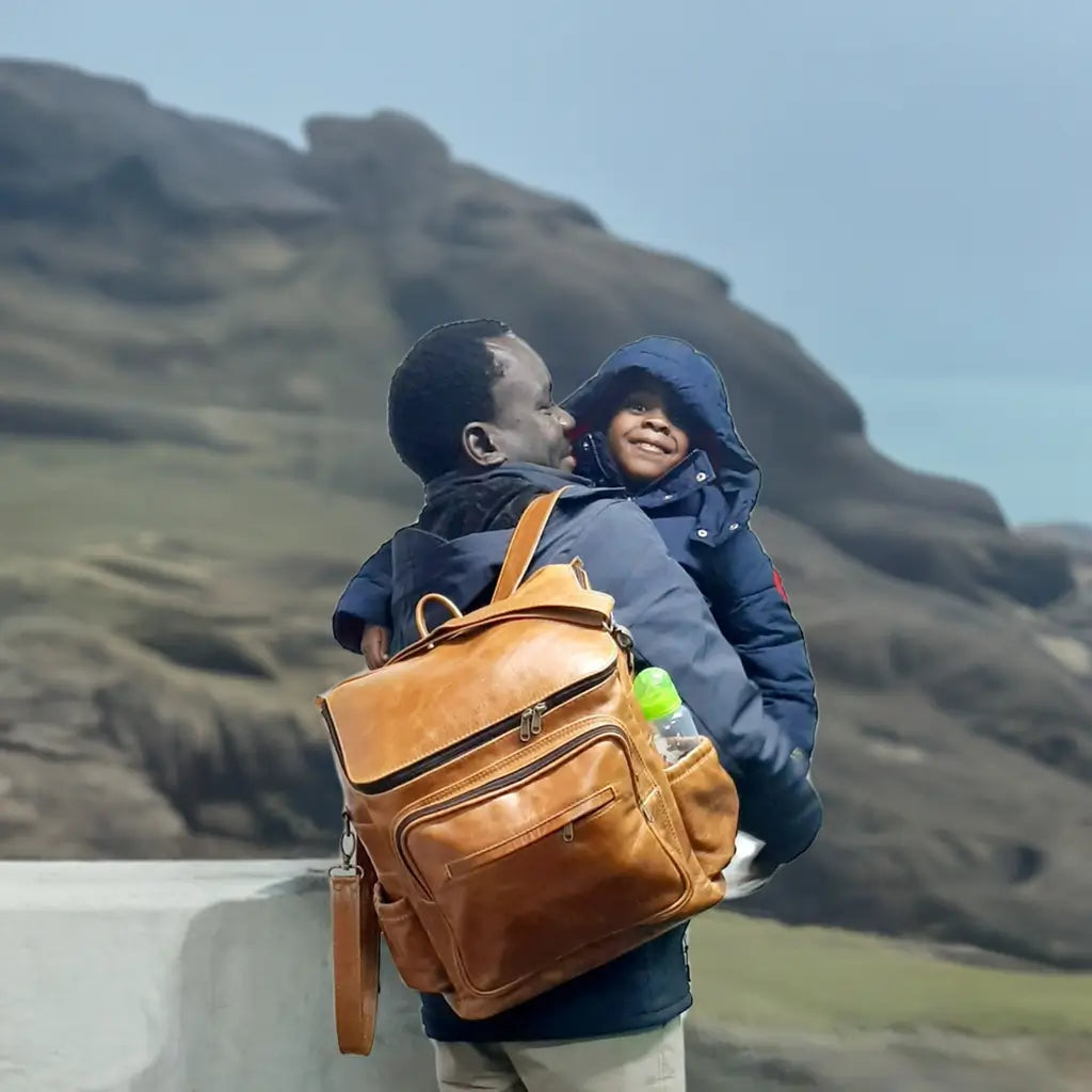A man carrying a baby and a beautiful baby backpack in light tan colour made by Cape Masai Leather