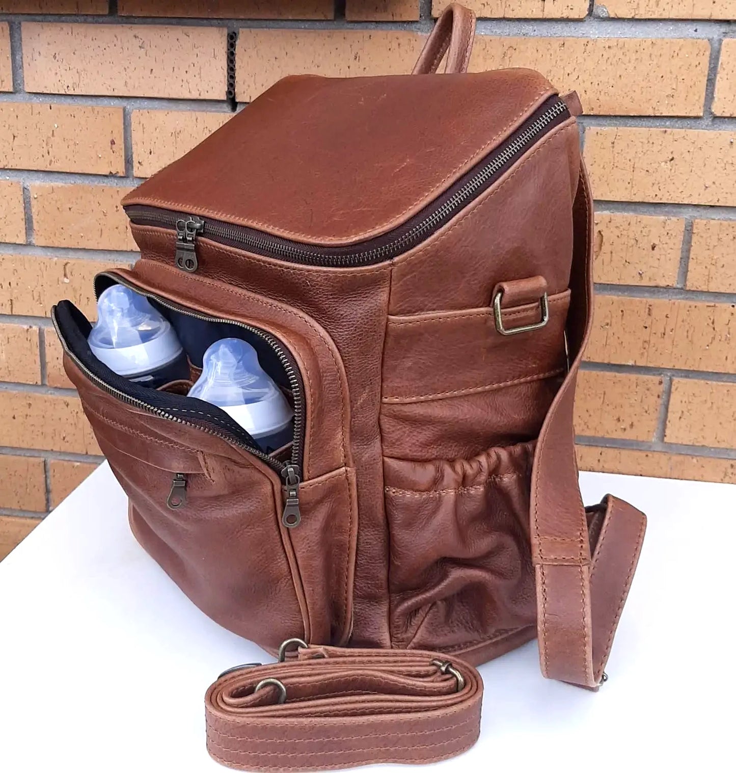 A beautiful baby backpack in Pecan tan colour made by Cape Masai Leather with 2 baby bottles in the front pocket