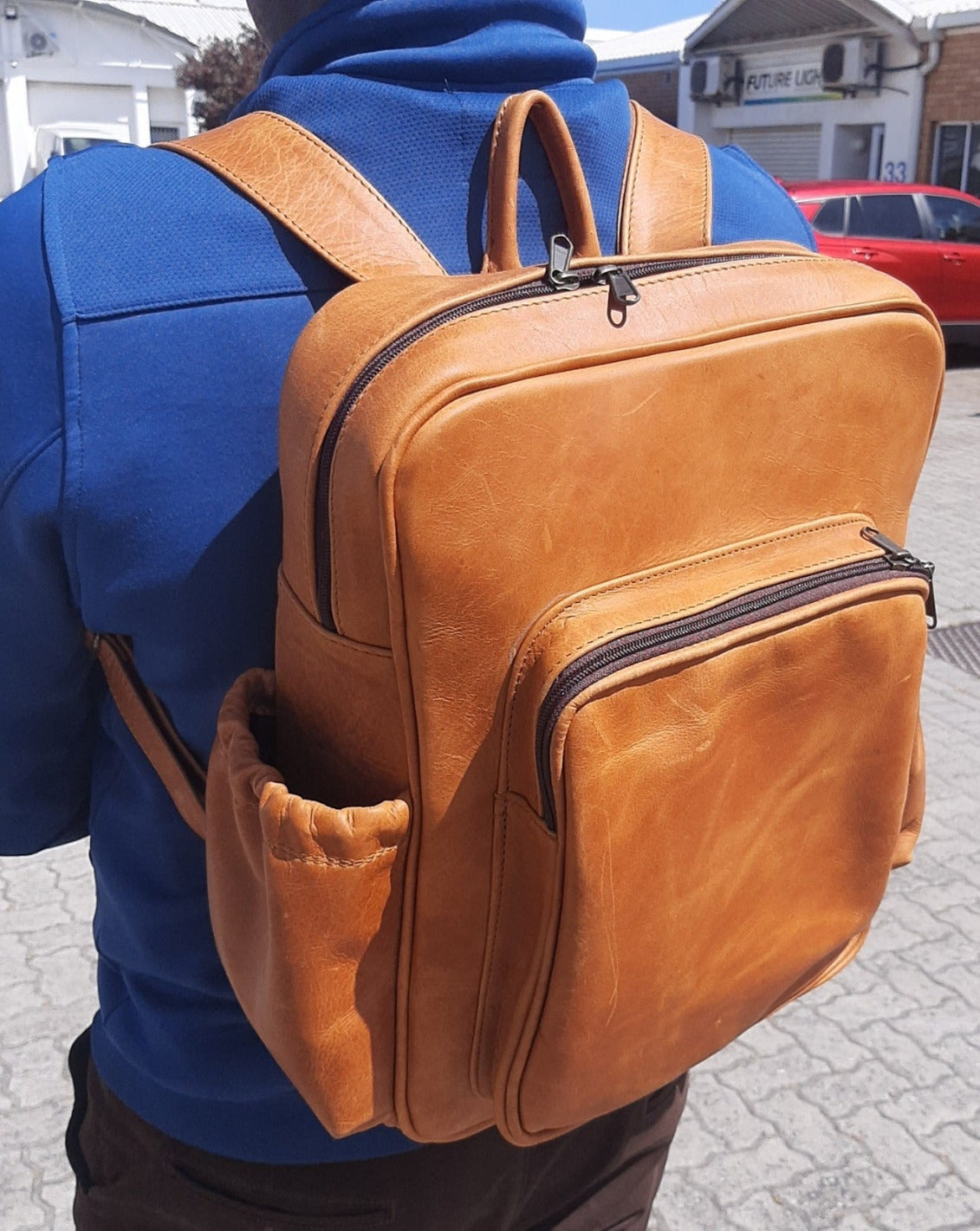 A man carrying geniune leather Everyday Laptop Backpacks 15" in Disiel Toffee tan with side pockets colour from Cape Masai Leather  