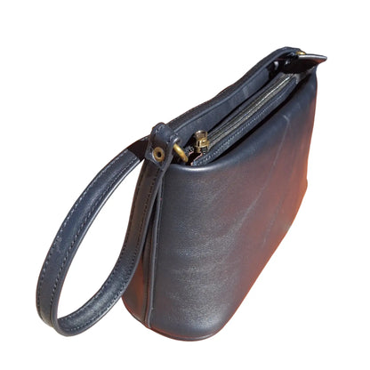 A black leather clutch handbag with a top zipper and wrist strap, resting on terracotta tiled outdoor steps.
