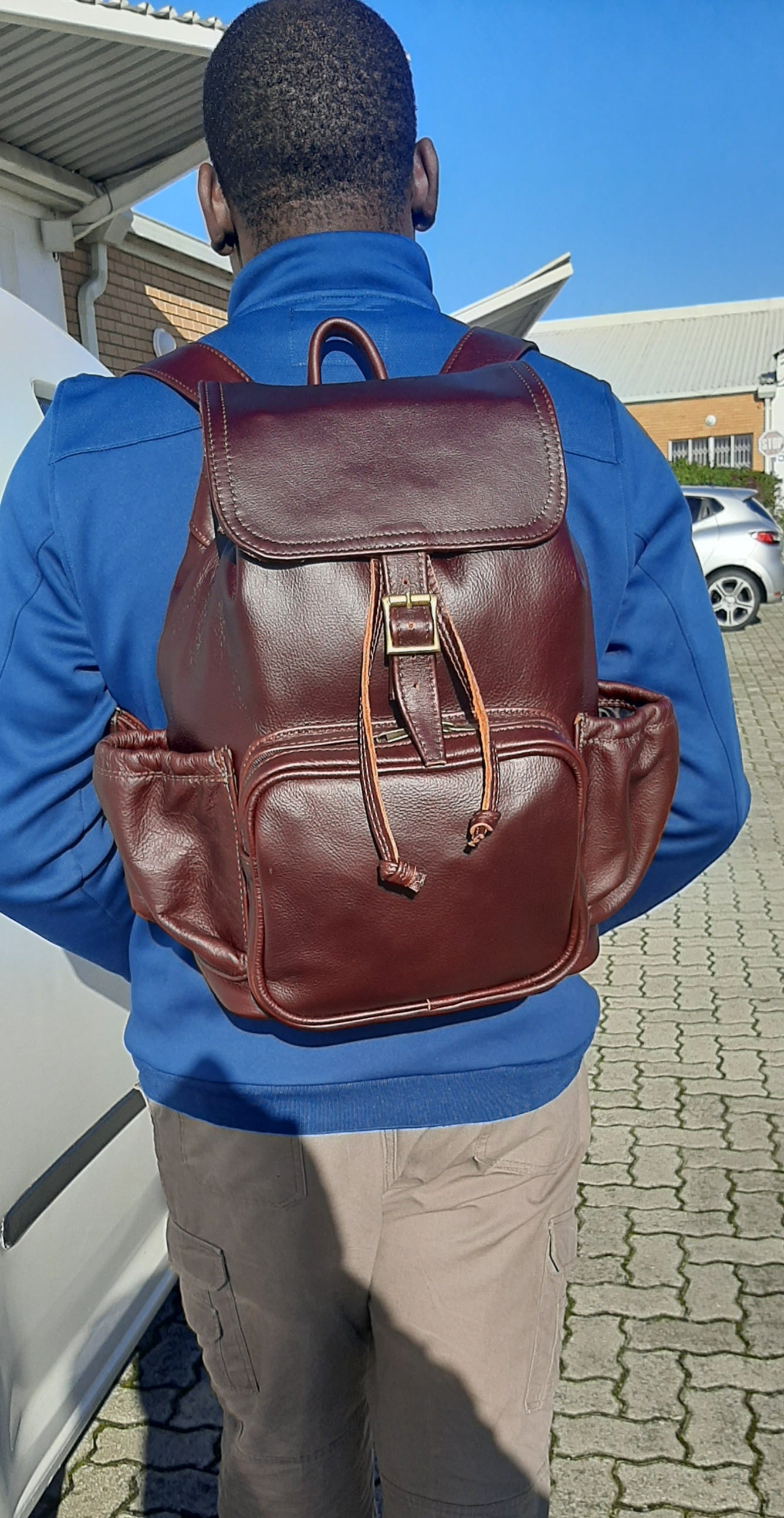 A man carrying  leather backpack with flap xl in dark tan colour on his back from Cape Masai Leath
