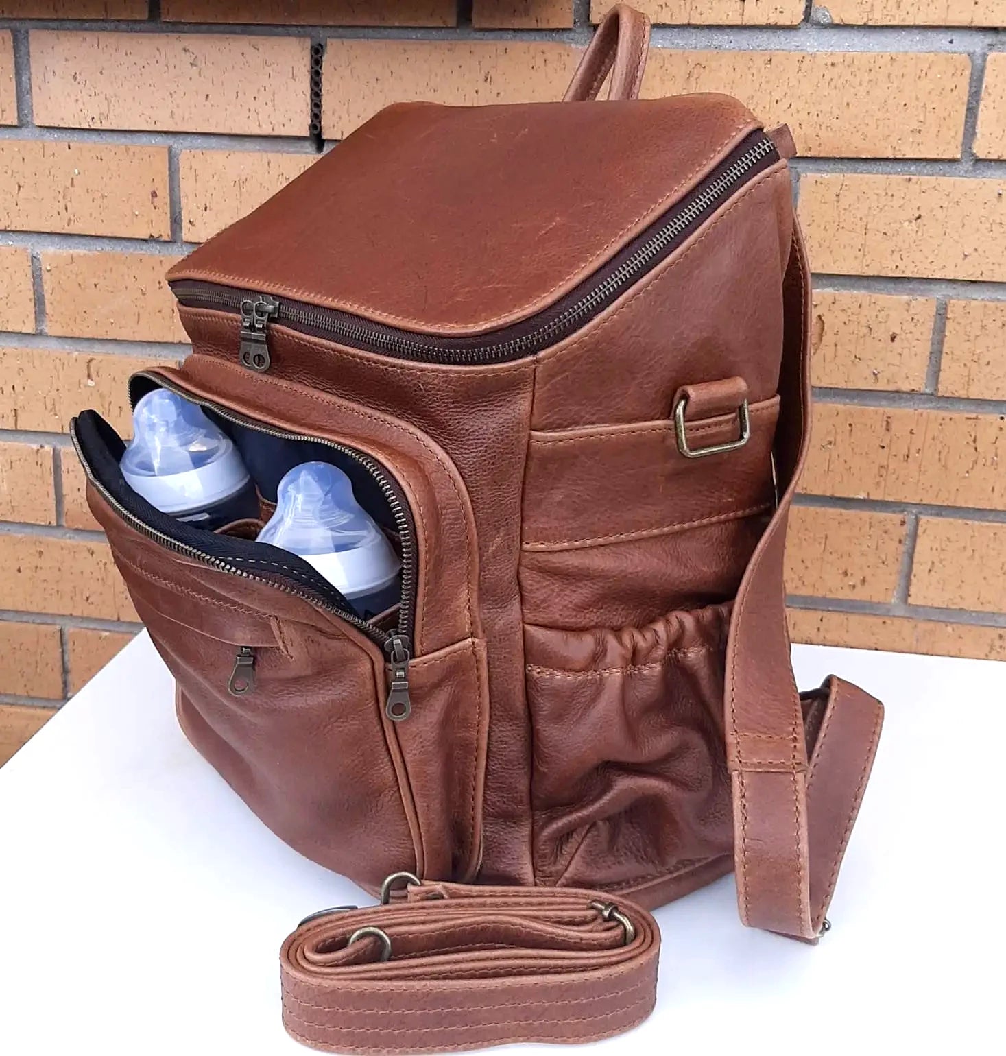 A beautiful baby backpack  in Pecan tan colour made by Cape Masai Leather with 2 baby bottles in the front pocket