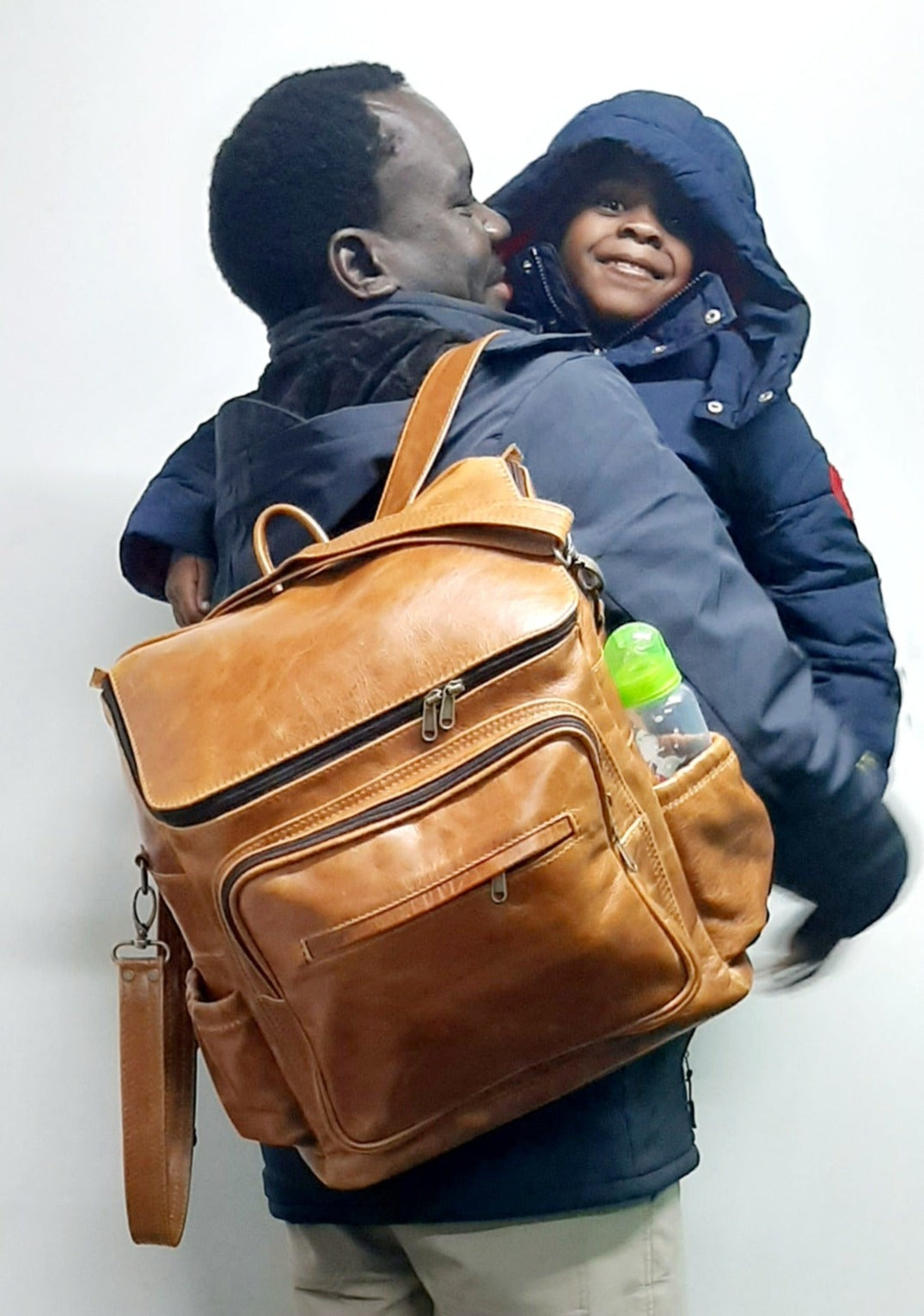 A man carrying a baby and a beautiful baby backpack in light tan colour made by Cape Masai Leather