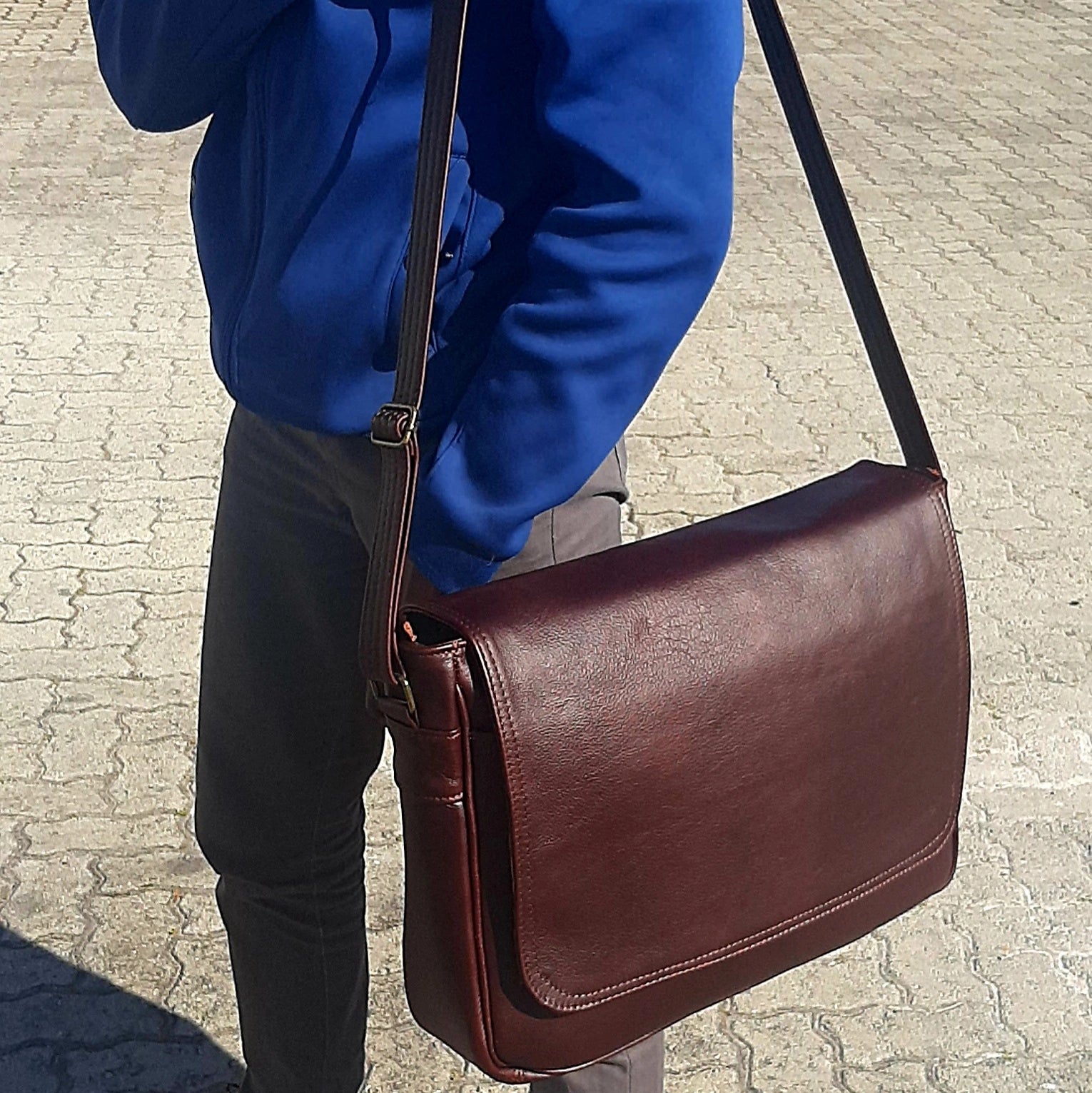 A young man carrying Men's laptop bag  15 - 15.6 inches dark tan outside Cape Masai Leather 