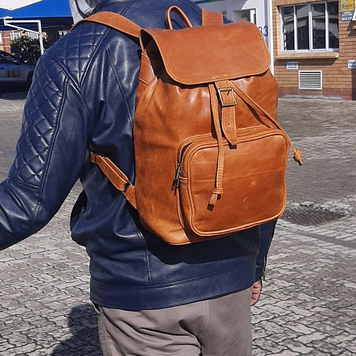 A gentle man carry toffe tan  leather backpack with flap xl without side pockets on his back outside Cape Masai Leather